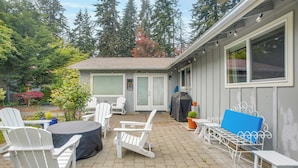 Une terrasse avec des meubles d’extérieur, un espace salon couvert et une vue sur une maison avec un garage.