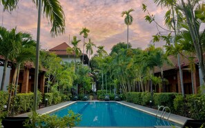 Ein Swimmingpool, umgeben von üppiger Vegetation und Palmen, mit einem Gebäude im Hintergrund.