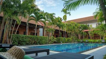 A poolside area with lounge chairs, a swimming pool, palm trees, and a building with a tiled roof.