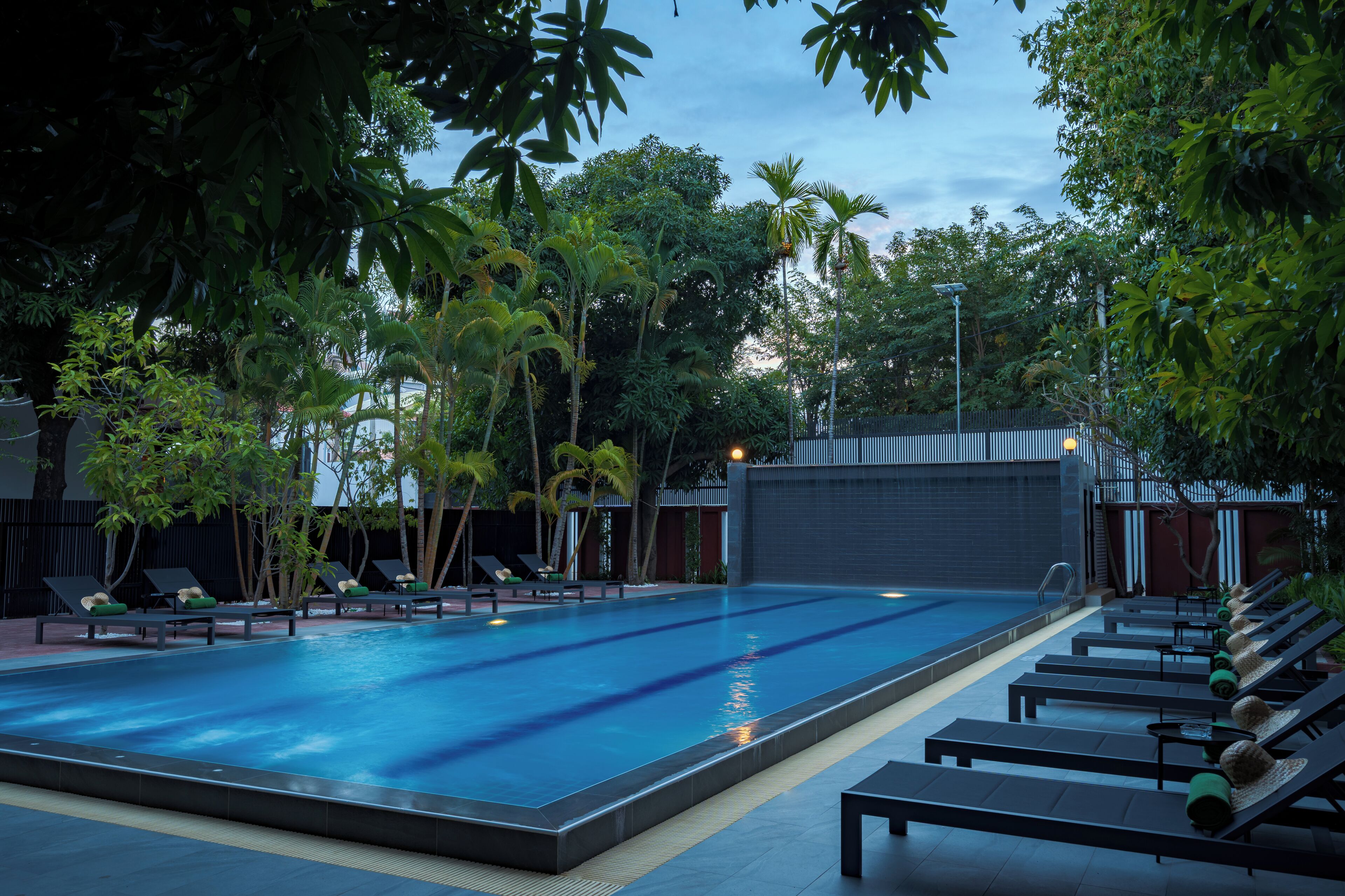 A swimming pool with lounge chairs, surrounded by trees and a building with a dark facade.