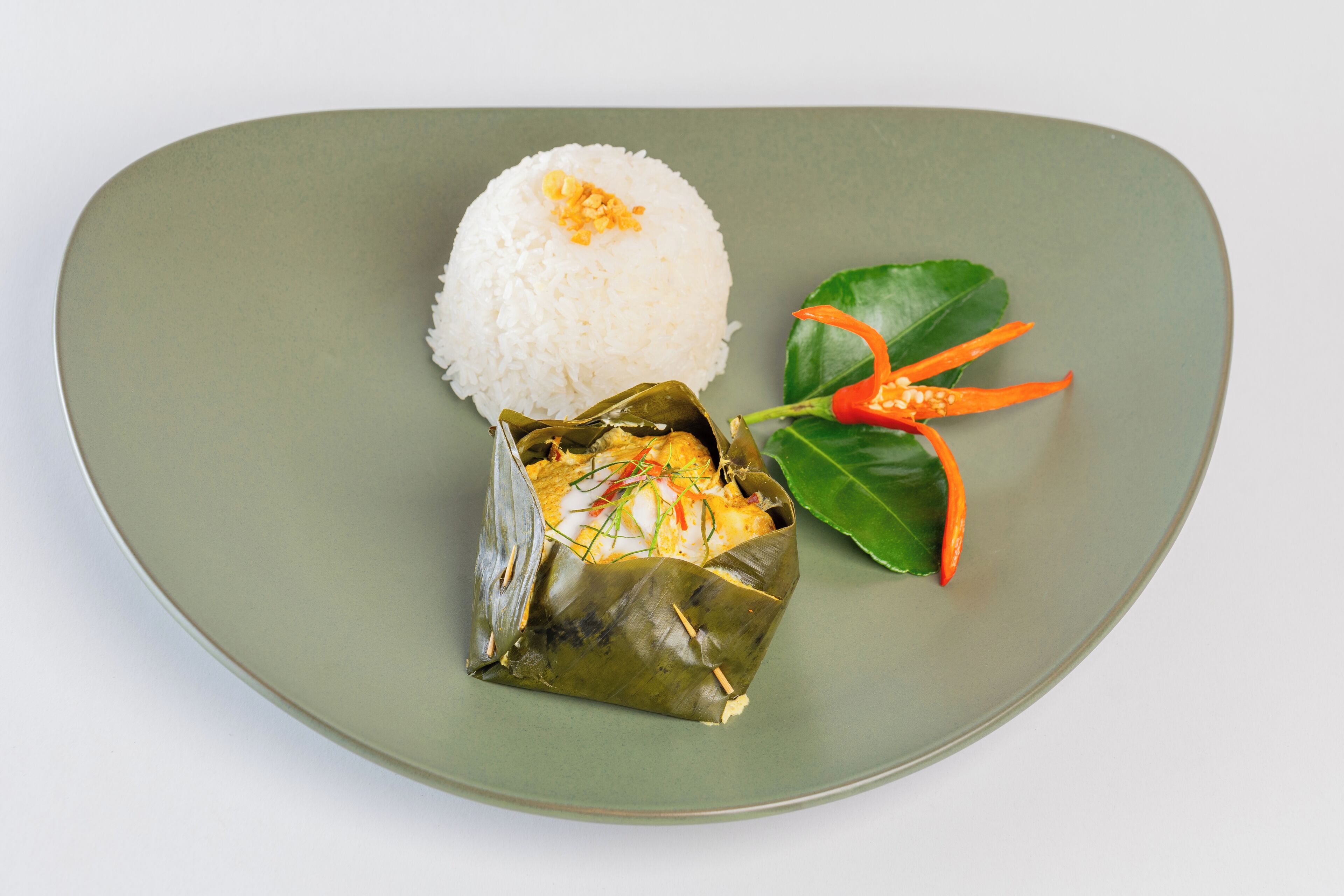 A plate with white rice, a wrapped food item, and a green leaf with red chili.