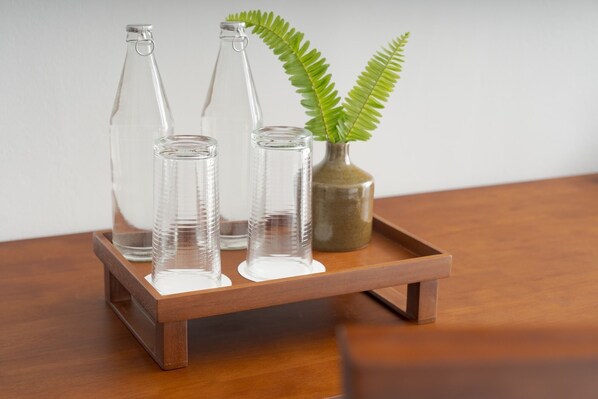 Three clear glass bottles on a wooden tray with a green plant in a vase. - Green Morodoc Garden Hotel (Siem Reap)