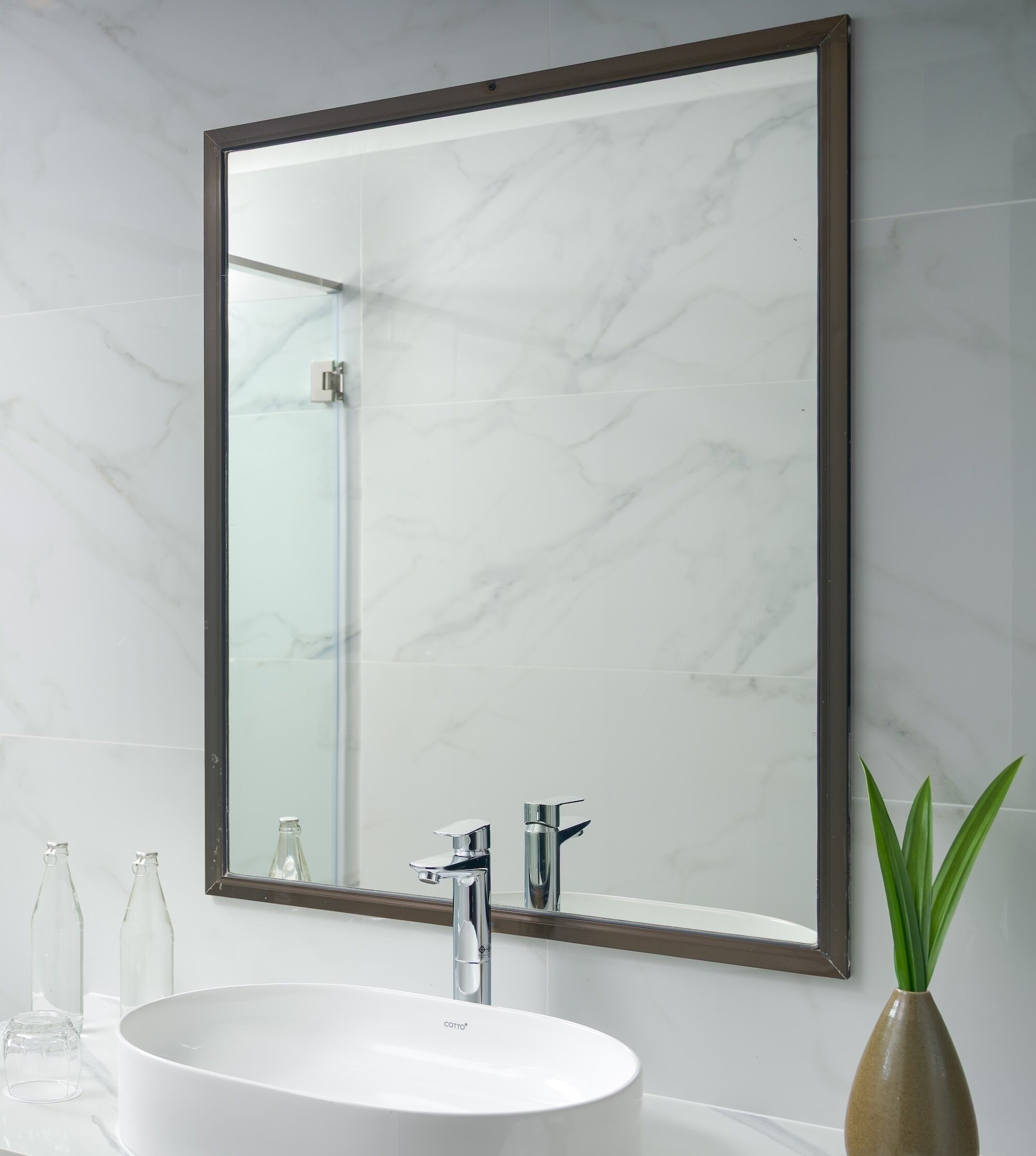 A bathroom with a white marble sink, a large mirror with a wooden frame, and a green plant in a vase.
