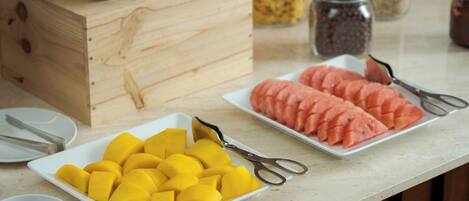 Una mesa de buffet con platos de mango y sandía en rodajas, una caja de madera y un tarro de especias.