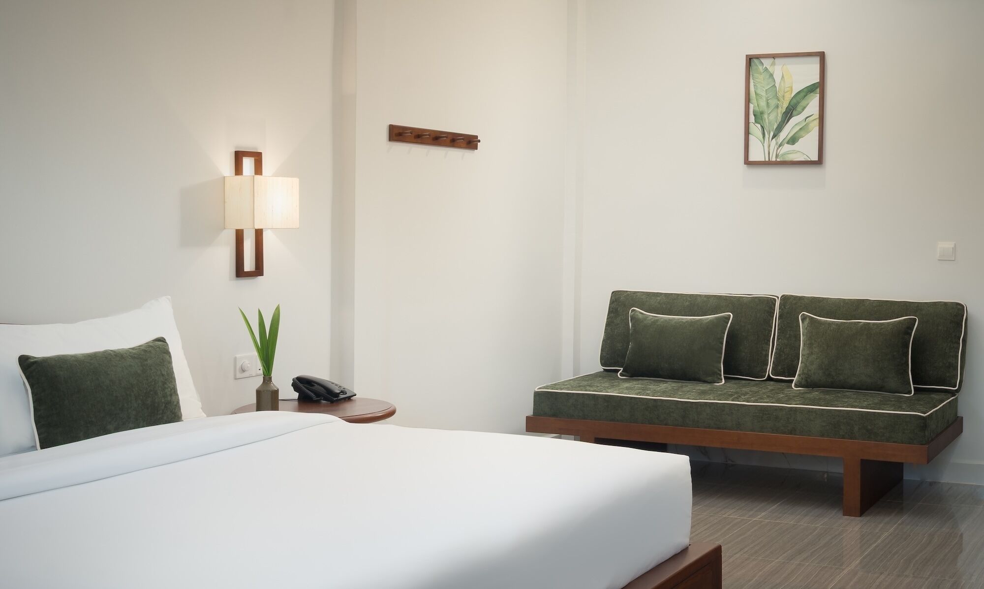 Una camera d'albergo con un letto, un divano, un comodino con una lampada e una pianta in vaso appesa al muro.