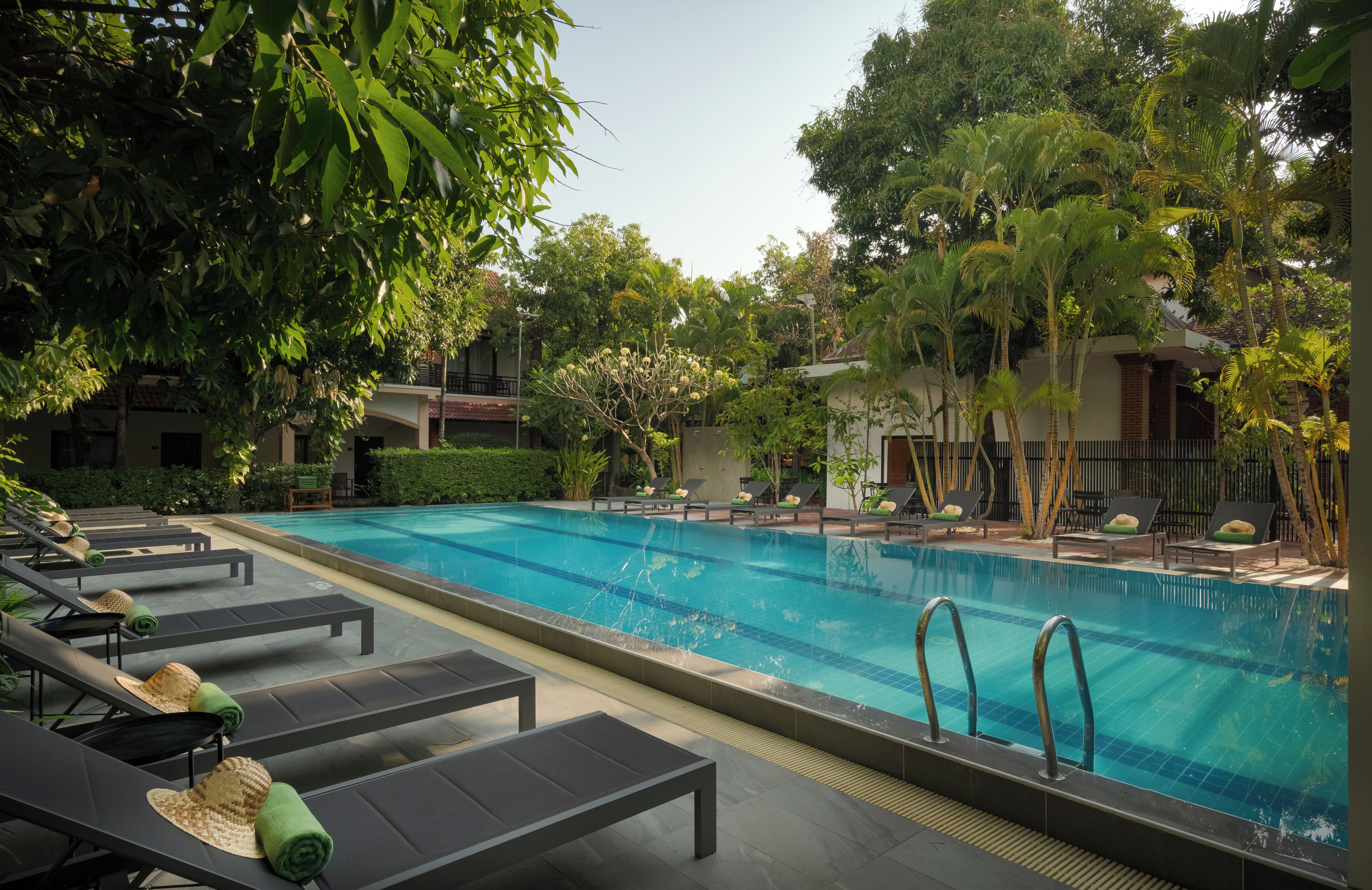Una piscina con sillas de descanso, rodeada de vegetación y edificios.
