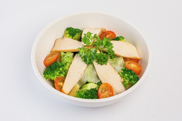Une salade composée de brocolis, de tomates et de morceaux de poulet.