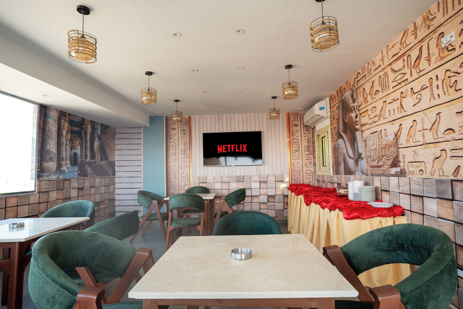Ein Restaurant mit grünen Polstersesseln, einem Tisch mit einer Metallschüssel und einer Wand mit Hieroglyphen.