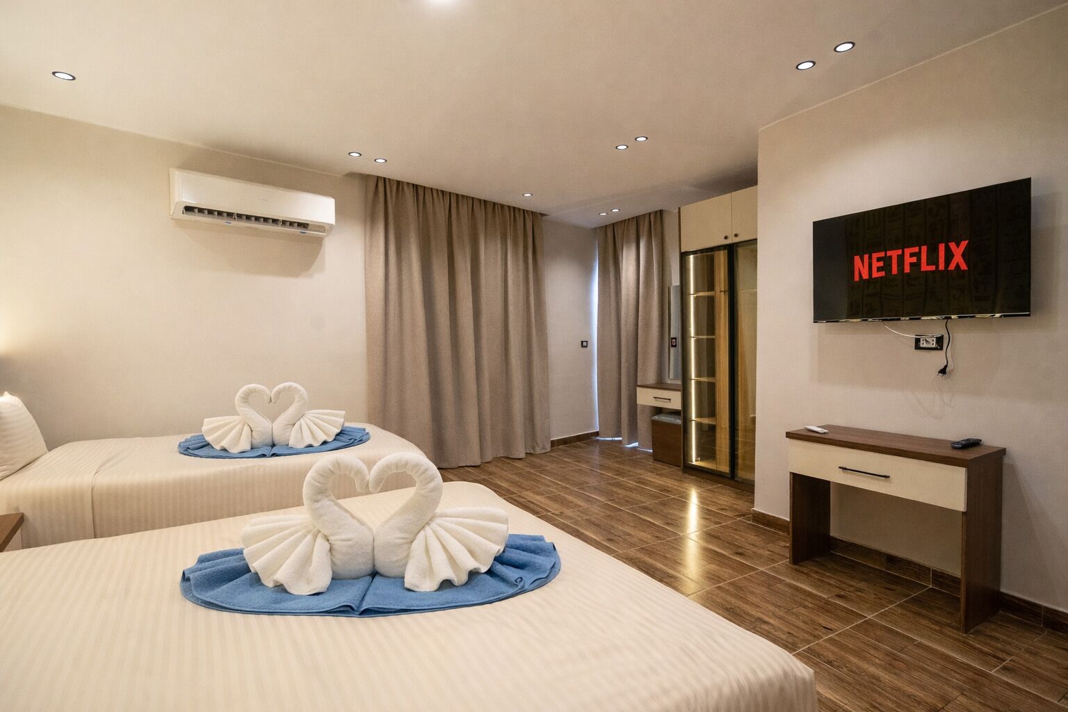 Une chambre d’hôtel avec deux lits, une télévision, un climatiseur et un bureau en bois.