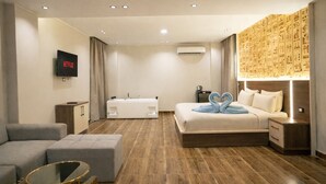A modern hotel room with a bed, a sofa, a small table, and a TV displaying the Netflix logo.