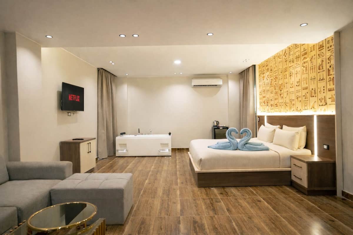 A modern hotel room with a bed, a sofa, a small table, and a TV displaying the Netflix logo.