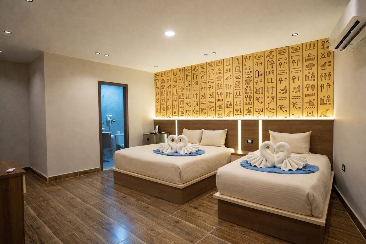 A hotel room with two beds, a wooden floor, and a wall decorated with hieroglyphs.