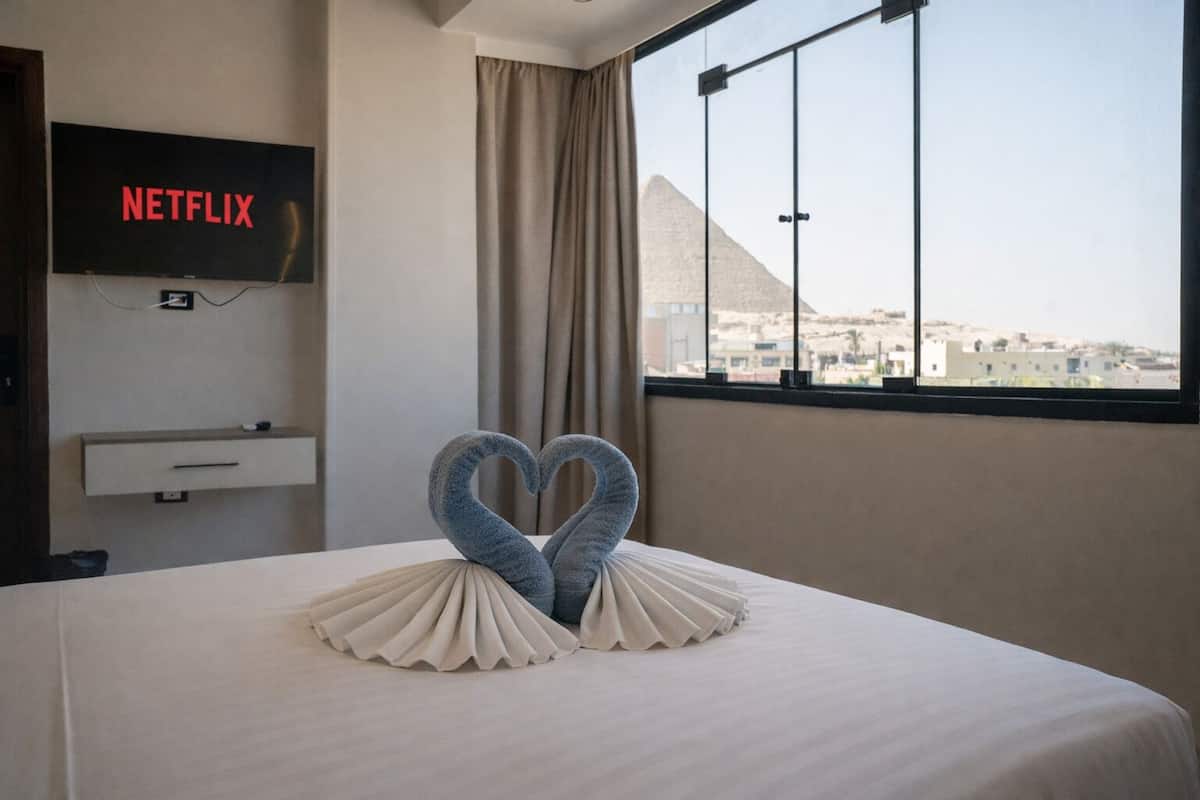 A hotel room with a bed, a TV displaying 'NETFLIX', a window with a view of a pyramid, and a decorative swan on the bed.