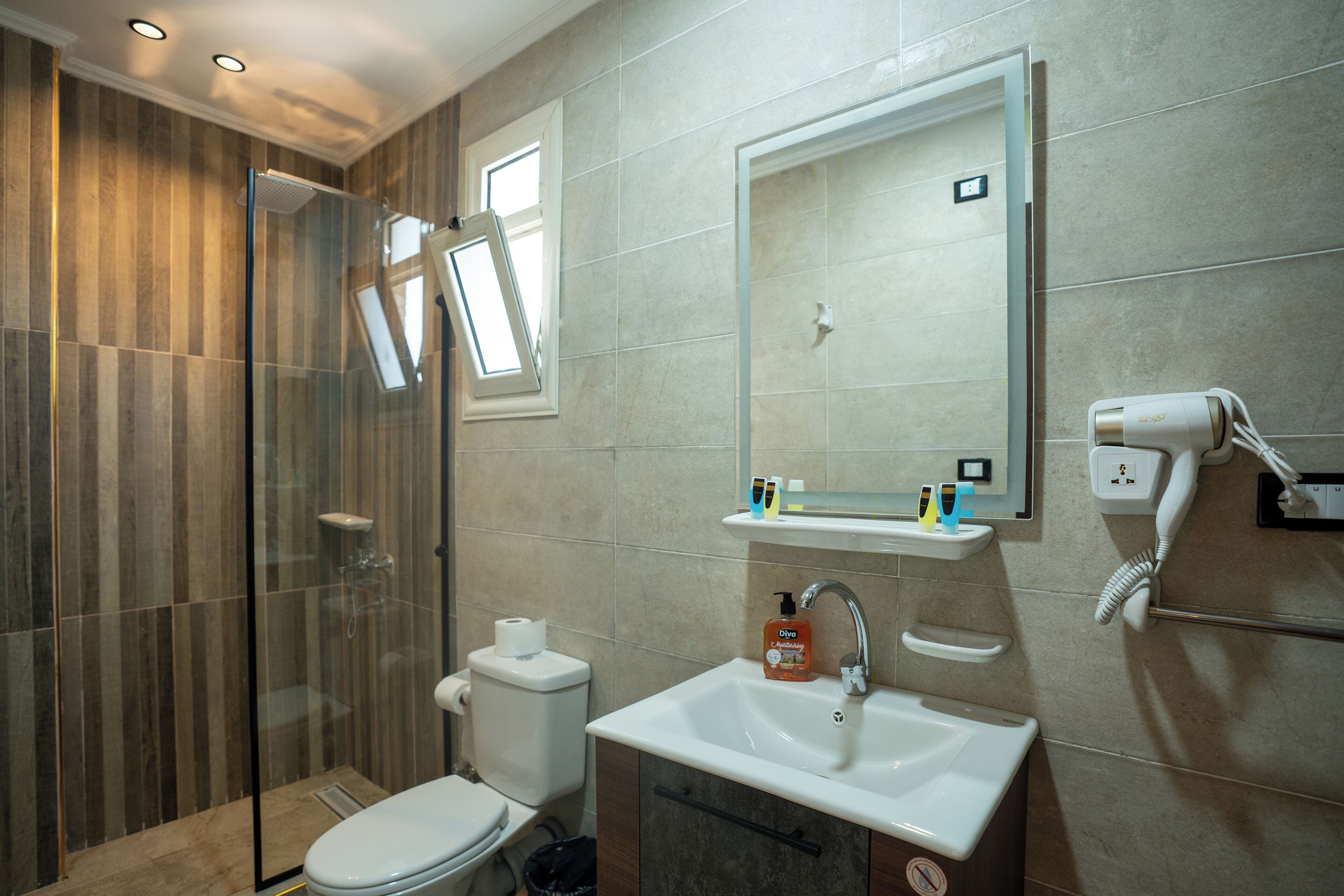 A modern bathroom with a glass shower enclosure, a toilet, a sink with a mirror above it, and a hairdryer on the wall.