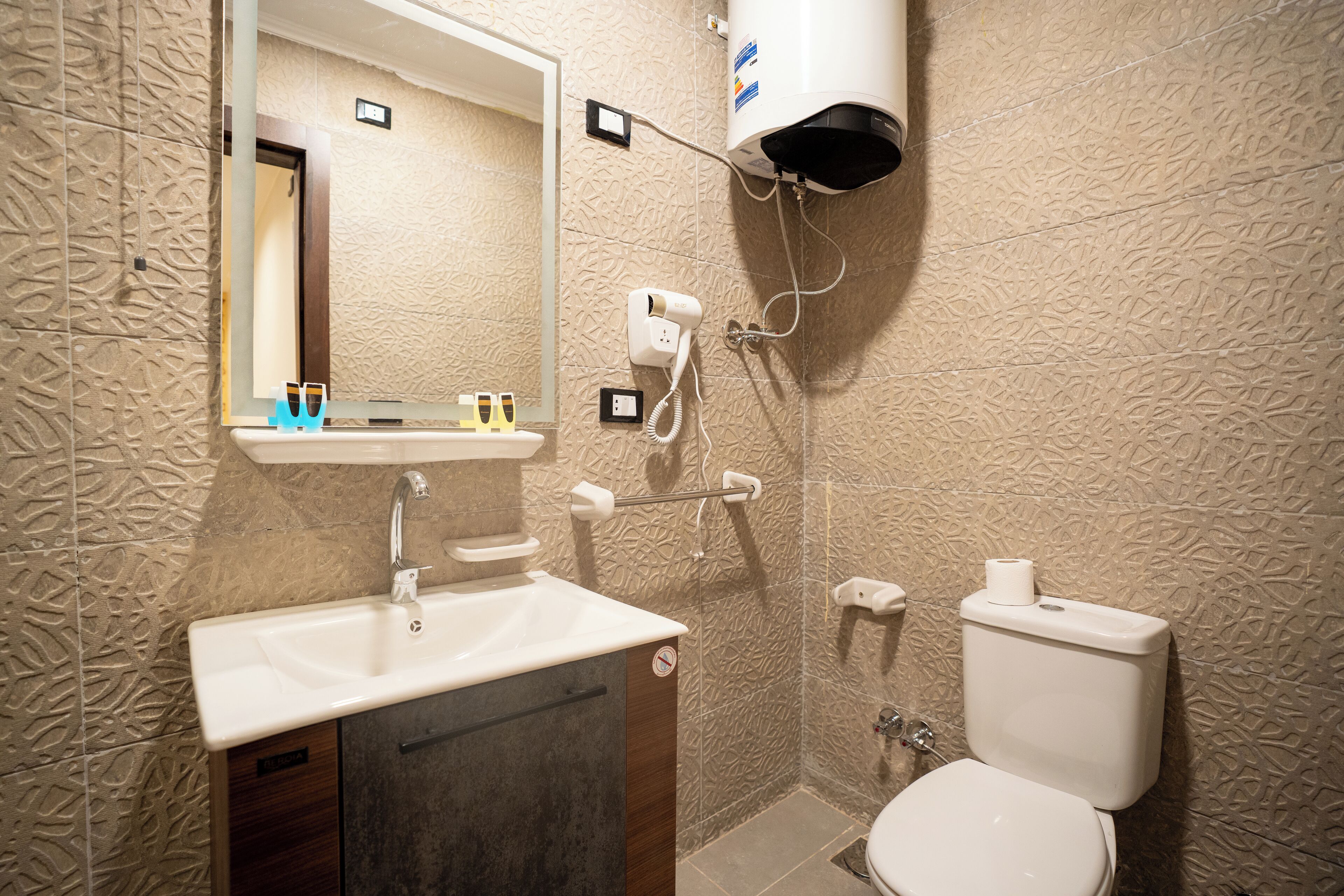 A bathroom with a sink, mirror, hairdryer, and toilet.