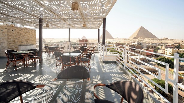 A rooftop terrace with outdoor seating, a view of the pyramids, and a white railing.