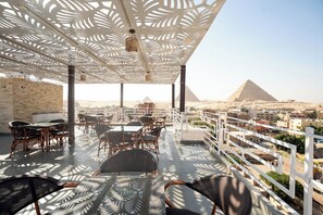 Une terrasse sur le toit avec des sièges extérieurs, une vue sur les pyramides et une rambarde blanche.