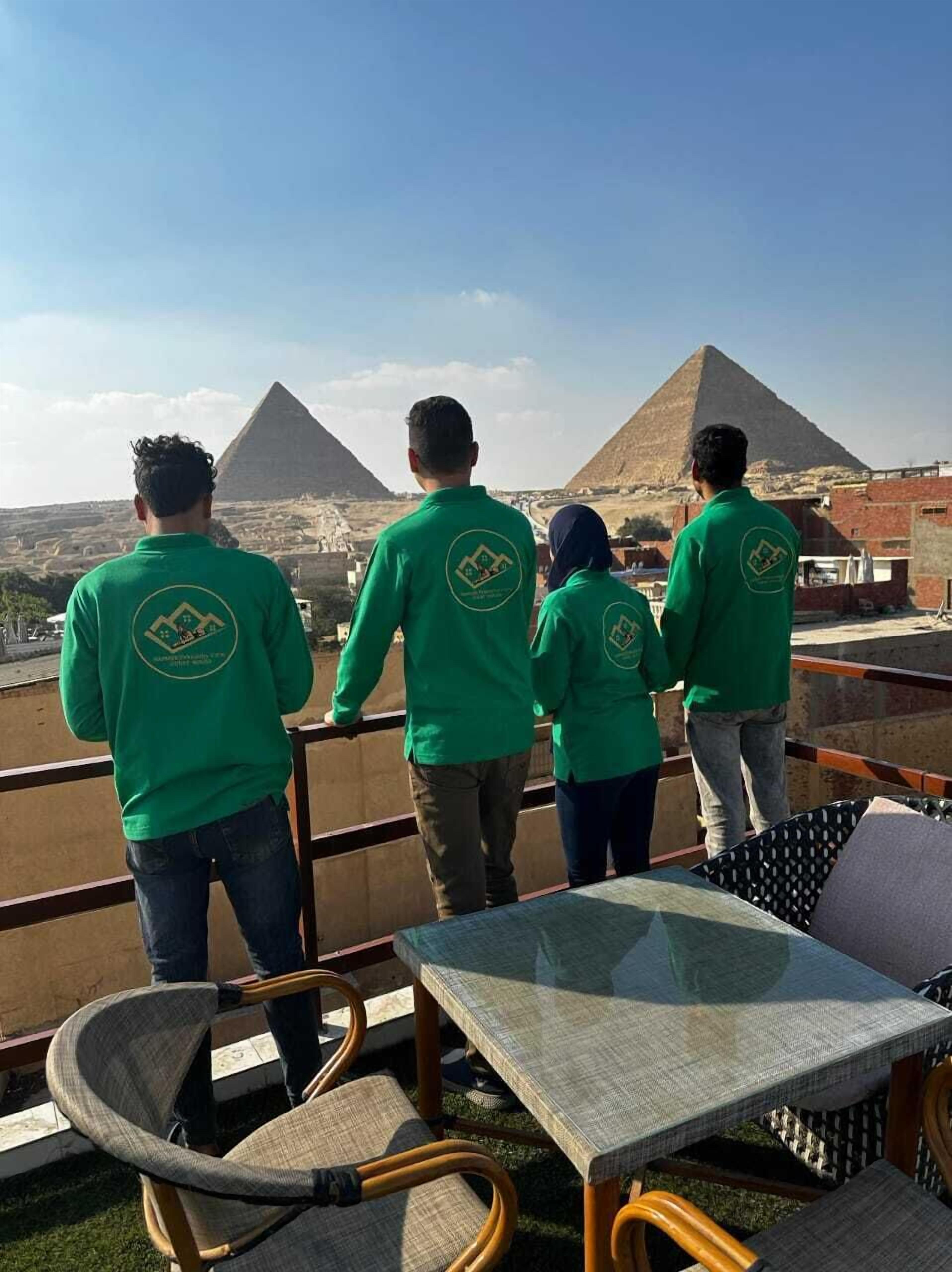 A group of people in green shirts standing on a balcony overlooking the pyramids.