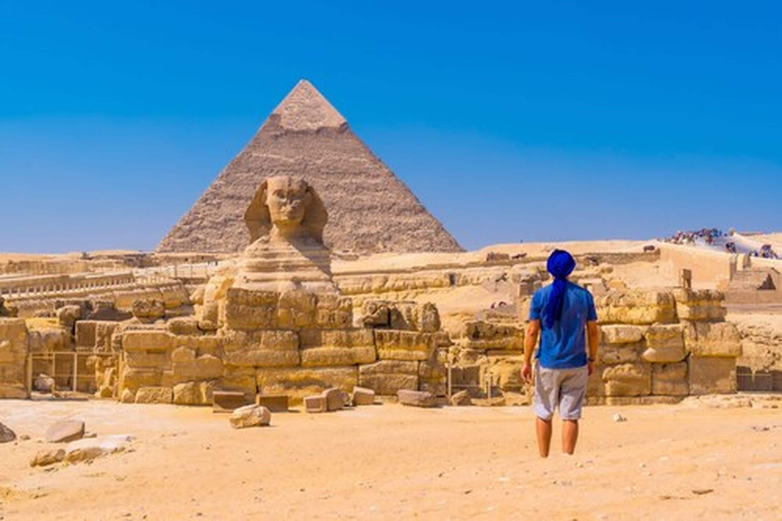 A person standing in front of the Great Pyramid of Giza with the Sphinx in the background.