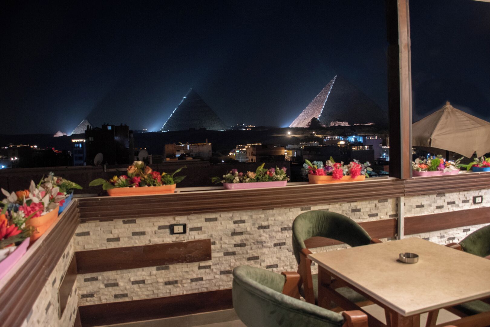 A rooftop terrace with a view of pyramids, outdoor seating, and potted plants.