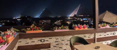 A rooftop terrace with a view of pyramids, outdoor seating, and potted plants.