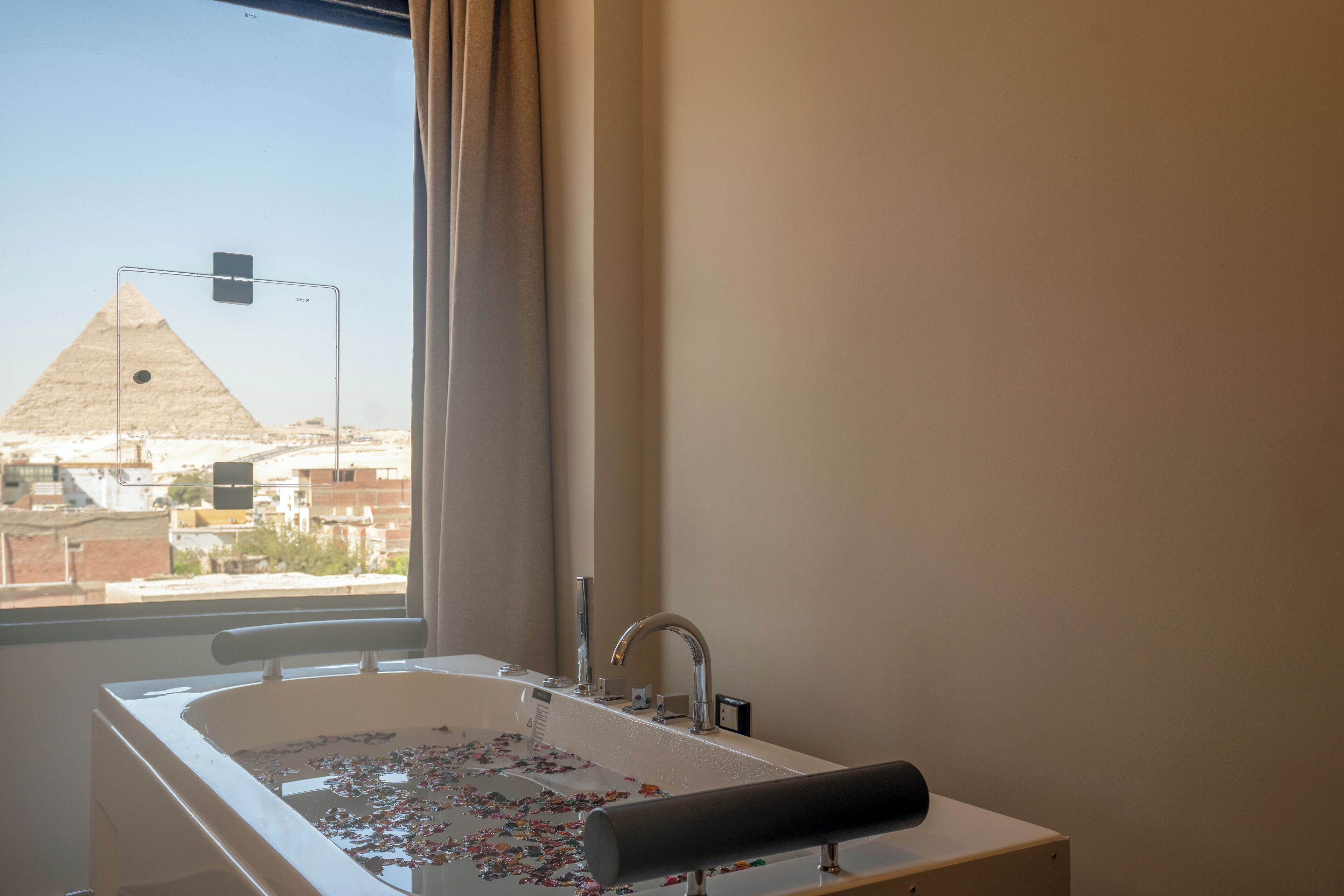 A bathroom with a bathtub filled with rose petals, a window with a view of a pyramid, and a curtain.
