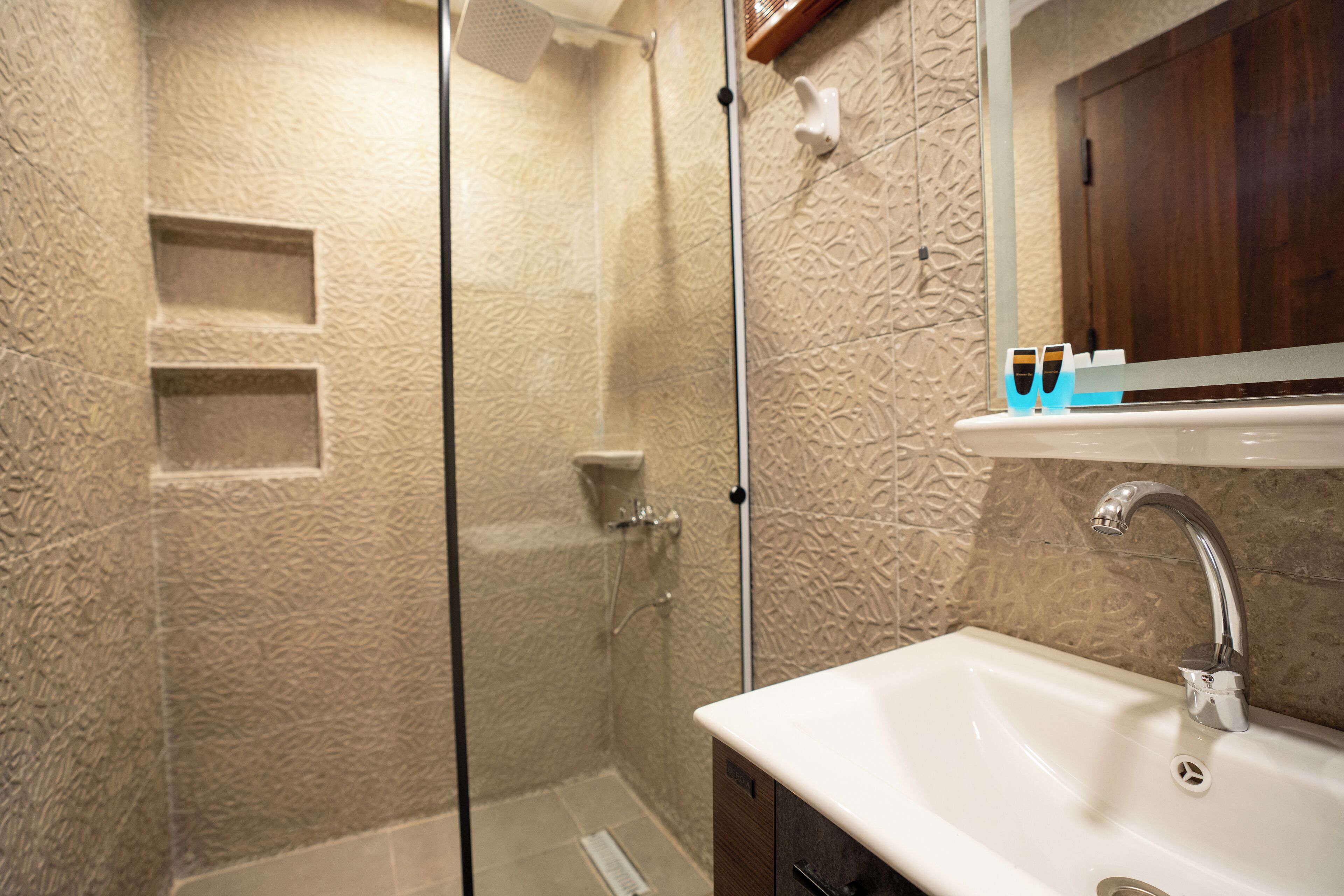 Un baño con ducha envuelta en vidrio, un lavabo blanco con un grifo moderno y un armario de madera sobre el lavabo.
