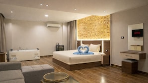 A modern hotel room with a large bed, a glass coffee table, a sofa, a vanity with a mirror, and a wall-mounted TV.