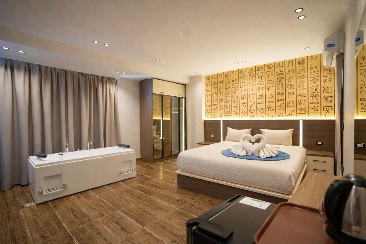 A modern hotel room with a large bed, a bathtub, and a wall with hieroglyphs.