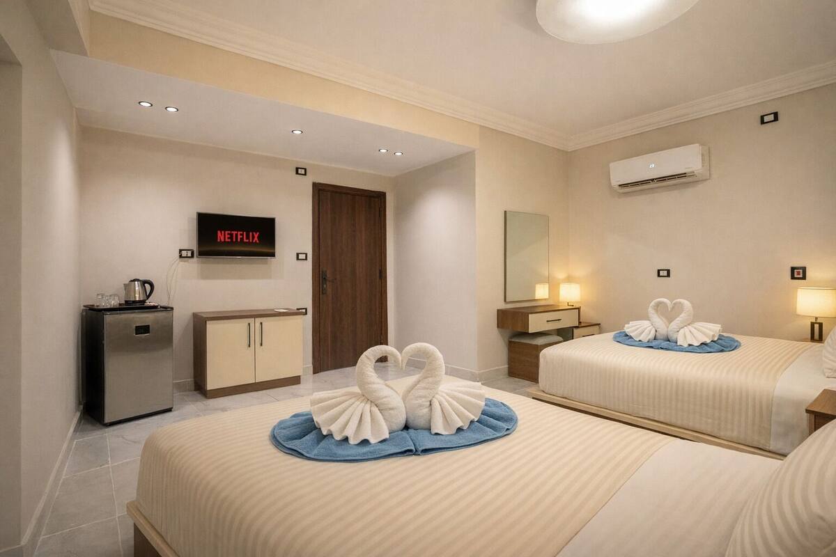 A hotel room with two beds, a minibar, a television, and a wall-mounted air conditioner.