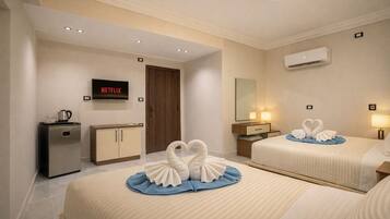 A hotel room with two beds, a minibar, a television, and a wall-mounted air conditioner.