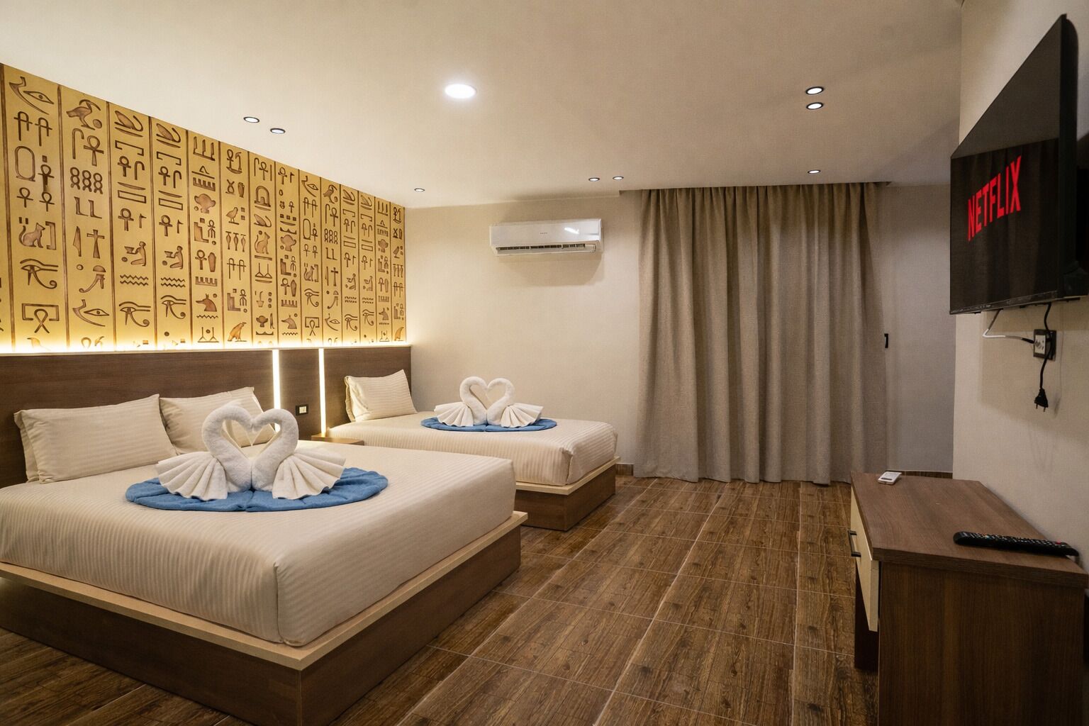 A hotel room with two beds, a TV, and a wall decorated with hieroglyphs.