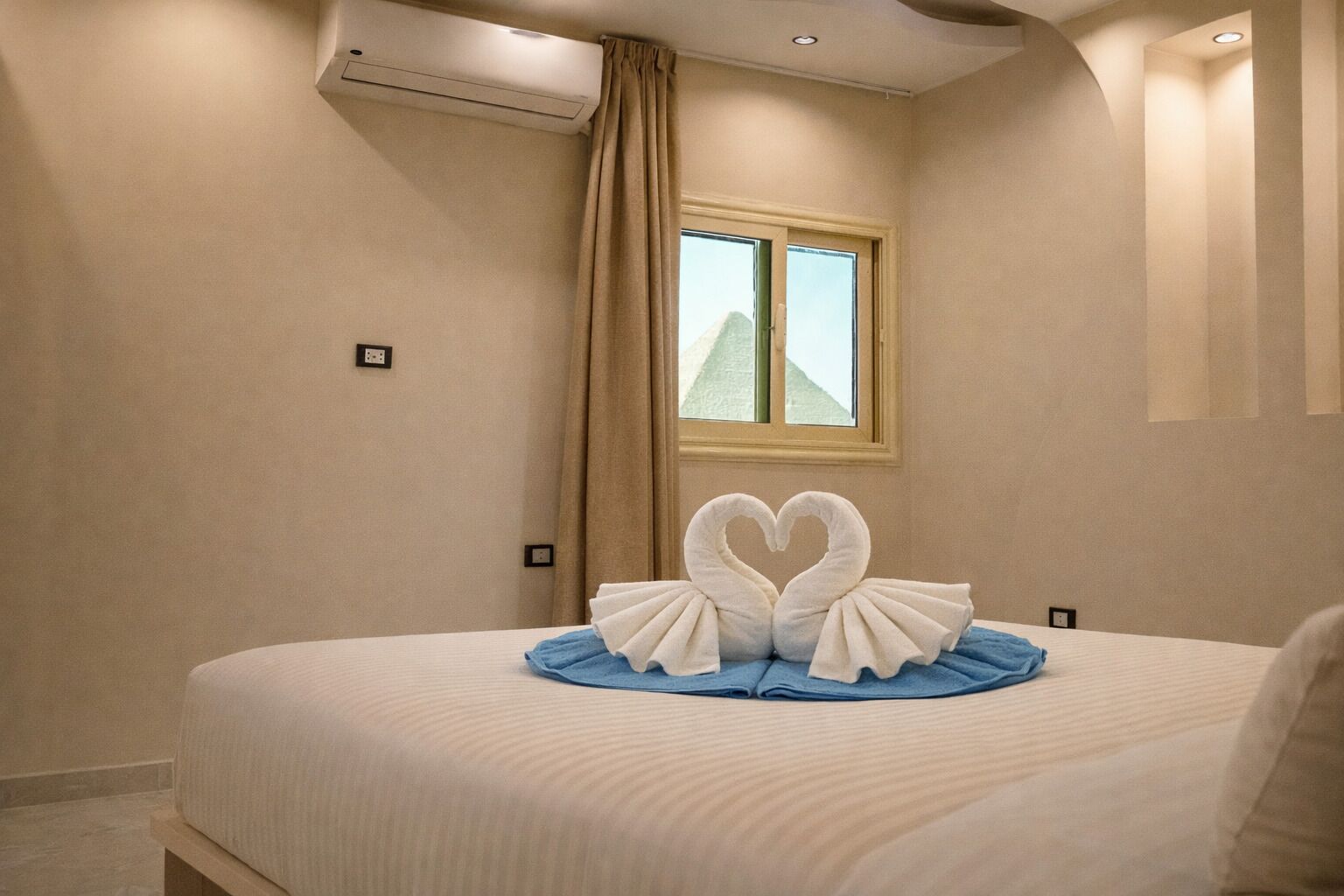 A hotel room with a bed, a window with curtains, and a wall-mounted air conditioner.