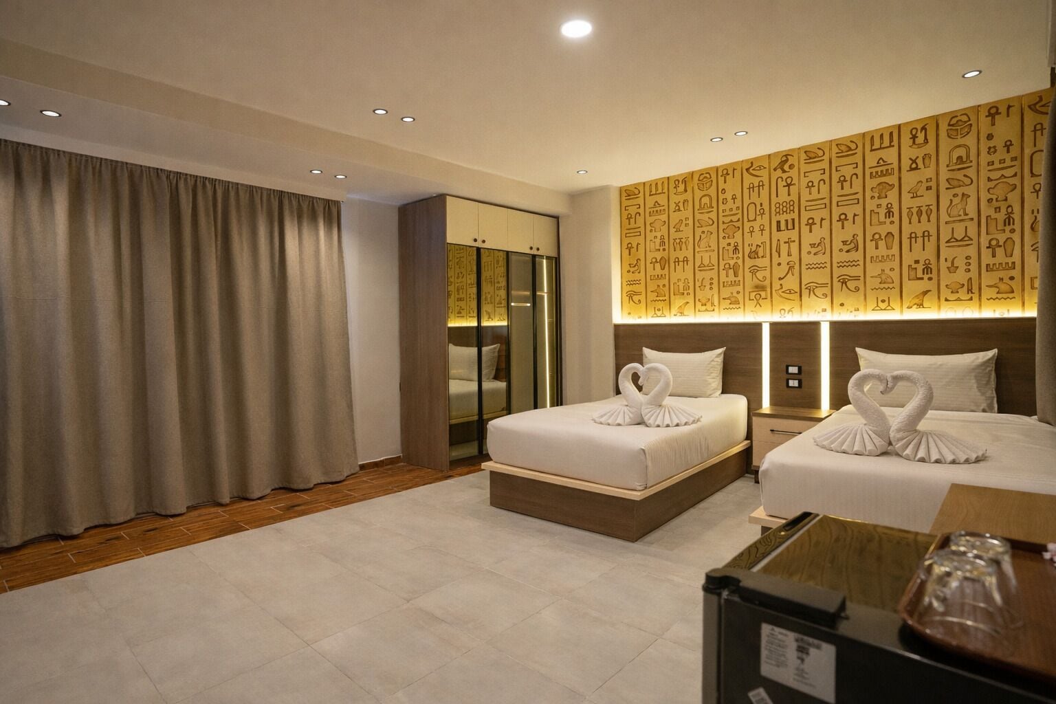 Habitación de hotel con dos camas, un armario y una pared con jeroglíficos.
