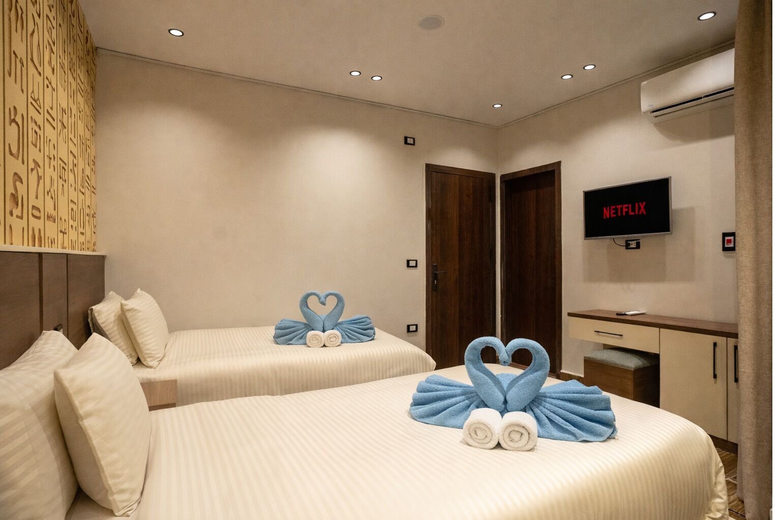 Ein Hotelzimmer mit zwei Betten, einem Fernseher und einer Wand mit Hieroglyphen.