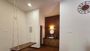 A hallway with a wooden swing, a round mirror, and a clock on the wall. - Acrewood Farmhouse - Pool Villa (Muvattupuzha)