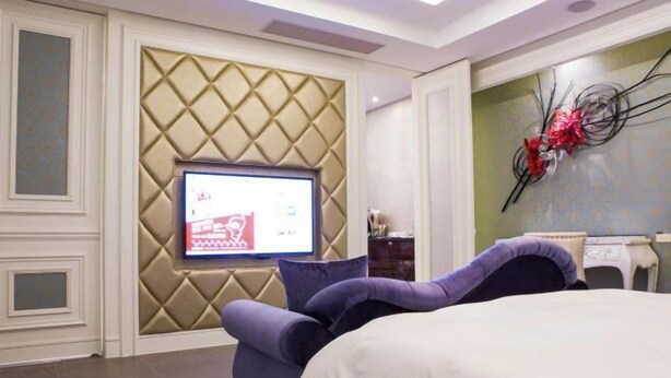 A modern hotel room with a bed, a television mounted on a textured wall, and a decorative wall piece. - ALL-UR Boutique Motel Hua-Lian Branch (Hualien)