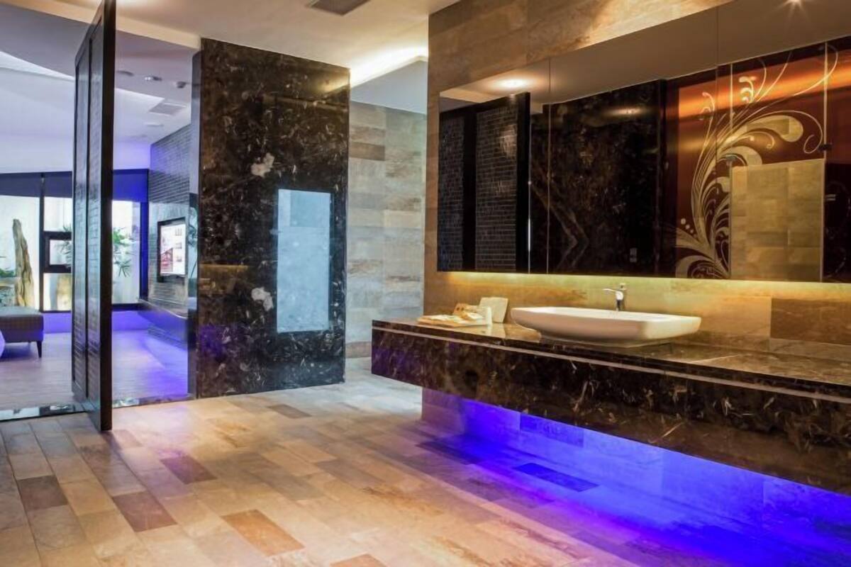 Ein modernes Badezimmer mit Marmorwaschbecken, einem großen Spiegel und einer blau beleuchteten Waschtischbank.