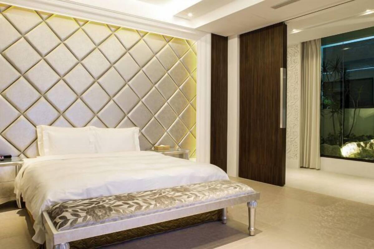 Ein modernes Schlafzimmer mit einem großen Bett, einer Bank, einem Nachttisch und einem großen Fenster mit Blick.