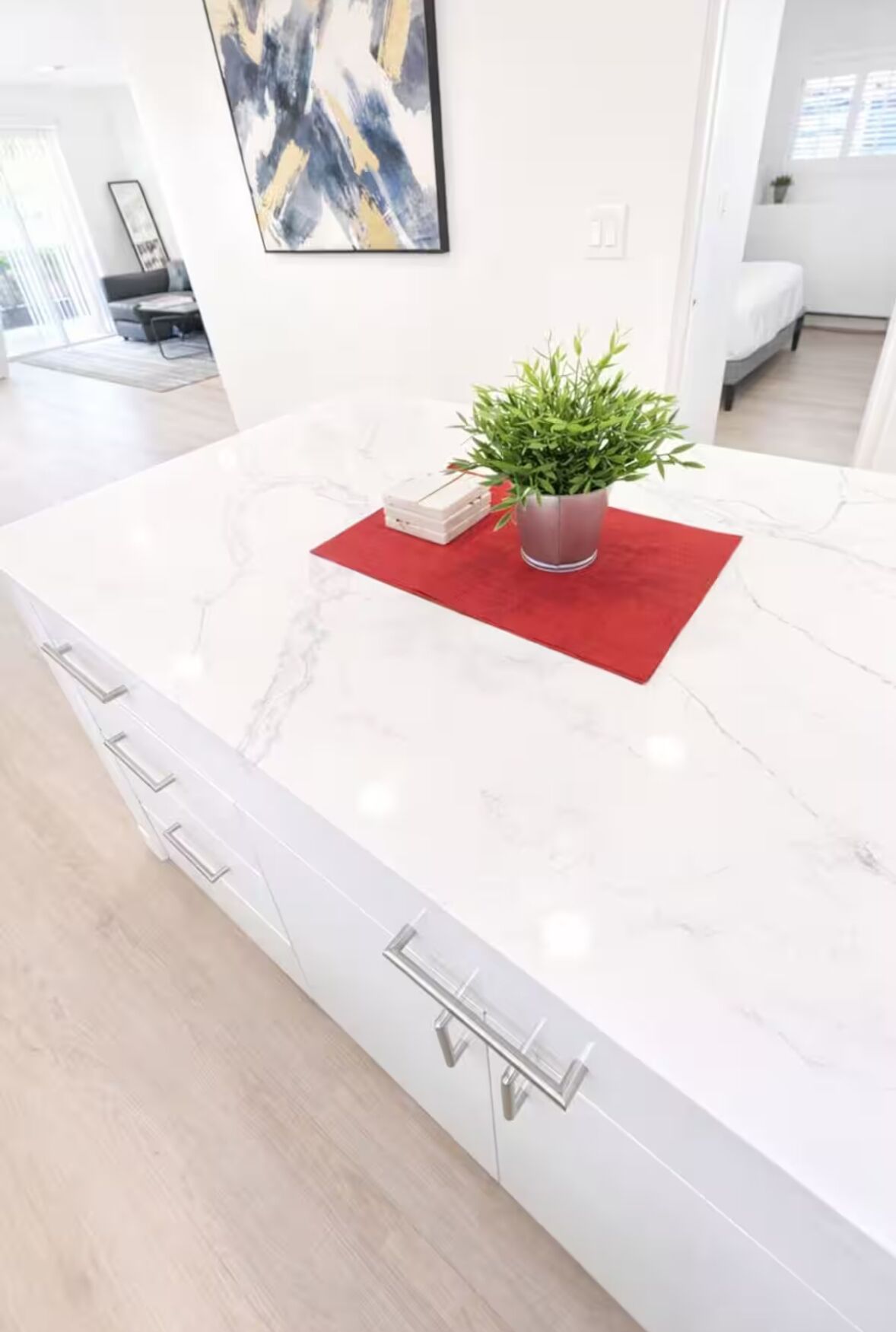 A modern kitchen with a marble countertop, a red placemat, a potted plant, and a set of drawers.