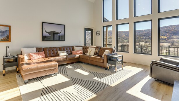 Uma sala de estar moderna com um sofá seccional grande, uma mesa de centro e vista para uma paisagem montanhosa através de grandes janelas.