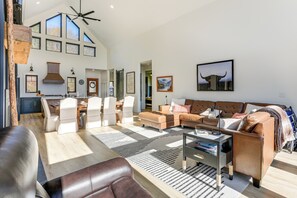 Een ruime woonkamer met een hoge plafond, grote ramen en een moderne keuken op de achtergrond.