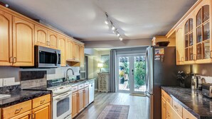 Een moderne keuken met houten kastjes, roestvrijstalen apparatuur en een groot raam dat uitkomt op een terras.