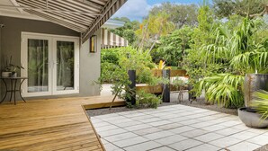 Een terras met een houten terras, betegeld gebied en diverse planten en bomen.