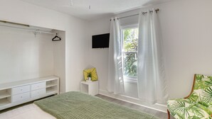 A bedroom with a bed, a white wardrobe, a small bedside table with a plant, a chair with a leaf pattern, and a window with curtains. - Fish, Swim & Boat: Riverfront Port Charlotte Home (Port Charlotte)