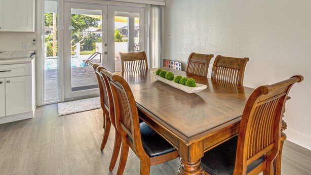 A dining area with a wooden table and chairs, a white cabinet, and a view of the outdoor area through glass doors. - Fish, Swim & Boat: Riverfront Port Charlotte Home (Port Charlotte)