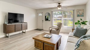 A living room with a flat-screen TV, wooden cabinet, beige sofa, and a ceiling fan. - Fish, Swim & Boat: Riverfront Port Charlotte Home (Port Charlotte)