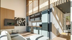 Ein modernes Wohnzimmer mit einer Couch, einem Fernseher und einer Küchenzeile mit Schränken und einer Arbeitsfläche.