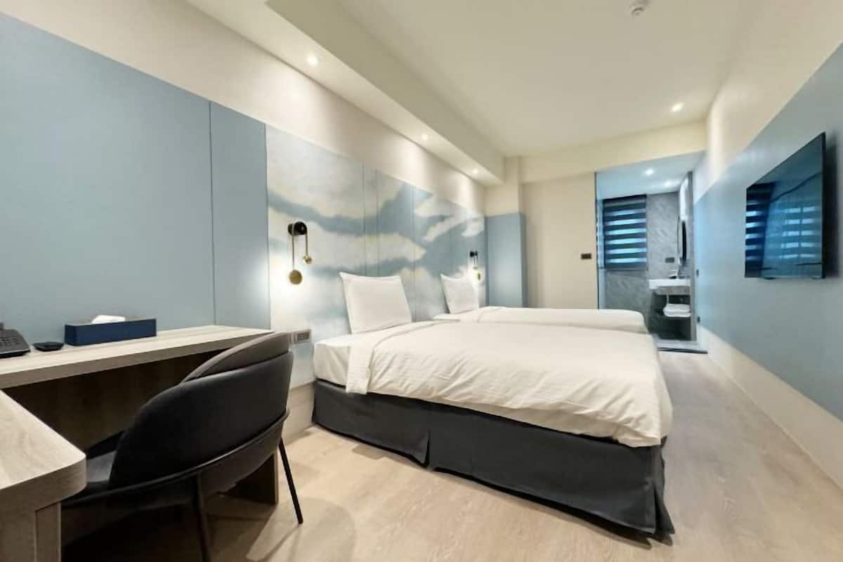 A modern hotel room with a bed, desk, chair, and a large mirror.