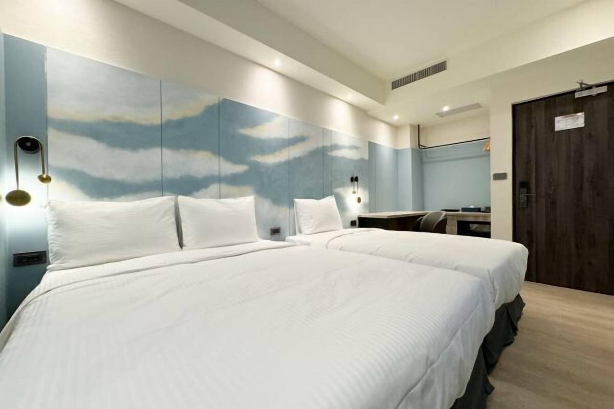 A hotel room with a large bed, a desk, a mirror, and a wall with a cloud mural.